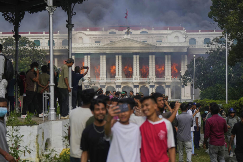Des jeunes Népalais se prennent en photo devant le siège du gouvernement népalais incendié par des manifestants à Katmandou, le 9 septembre 2025.