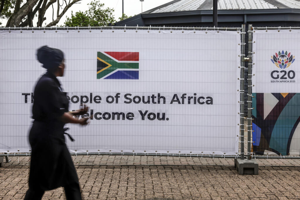 Une travailleuse passant devant une banderole arborant le drapeau sud-africain et le logo du G20 au Nasrec Expo Centre de Johannesburg, le 21 novembre 2025, à la veille du sommet des dirigeants du G20.