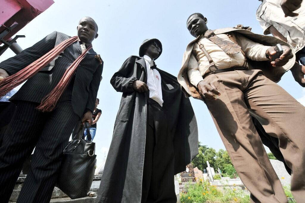 Deux sapeurs  de Brazzaville (de gauche à droite) et un Sapeur  de Kinshasa (au centre) rendent hommage à Stervos Niarcos, le 10 février 2013, à l'occasion du 18e anniversaire de sa mort, au cimetière de Gombe à Kinshasa. Niarcos   le fondateur de la religion « Kitendi », qui signifie « vêtements » en lingala.