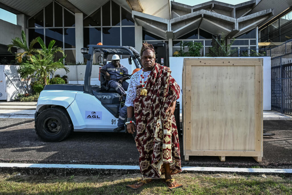 Un chef traditionnel de la tribu Ebrié posant à côté d'une caisse contenant le tambour Djidji Ayokwé, lors de son arrivée à l'aéroport international Félix Houphouët-Boigny d'Abidjan, le 13 mars 2026.